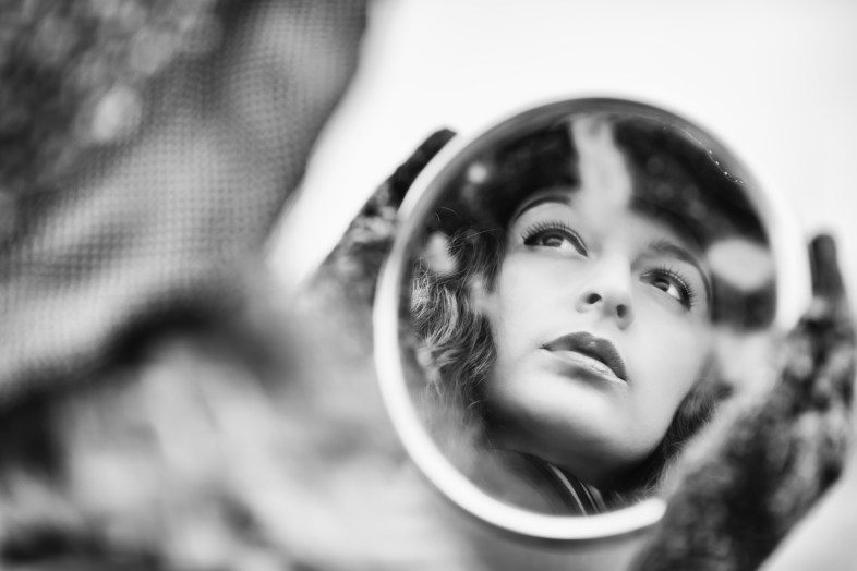 Face's reflection on mirror of beautiful pensive woman, retro styled image in black and white.