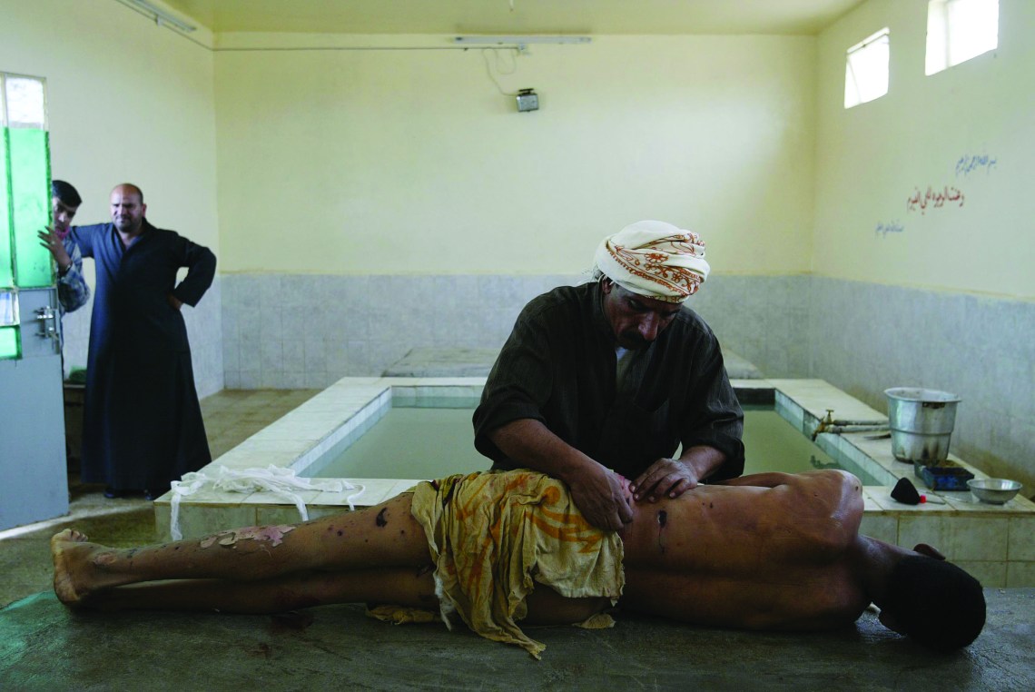 FILE -- In this photo by Joan Silva, Ali Hadi, a professional body washer, prepares the body of a bombing victim for Muslim burial as the man's relatives watch in Najaf, Iraq, on March 3, 2004. Silva was severely wounded on Oct. 23, 2010, when he stepped on a mine while on patrol with American soldiers in southern Afghanistan. (Joao Silva/The New York Times)