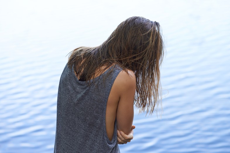 Rearview of a woman hugging herself with rippled water in the background