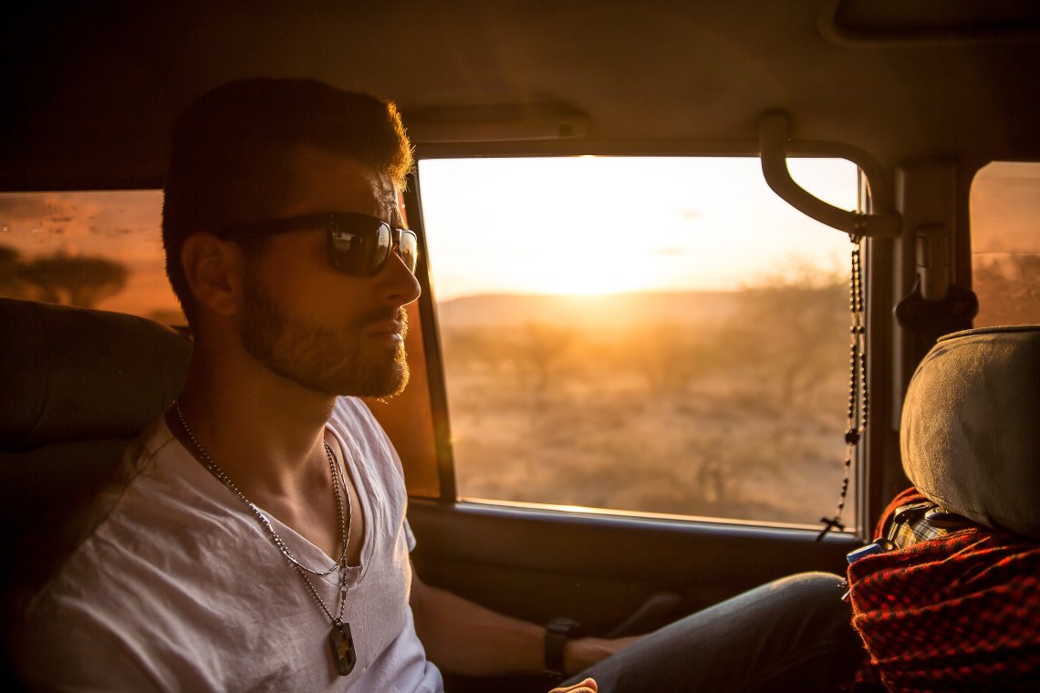 Handsome man riding in car, sunset behind him. 