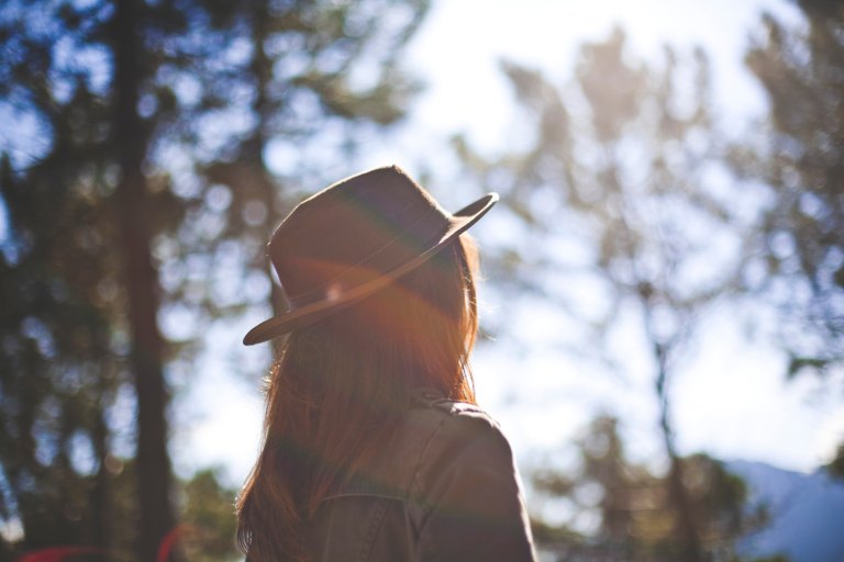 Woman with fedora standing by trees