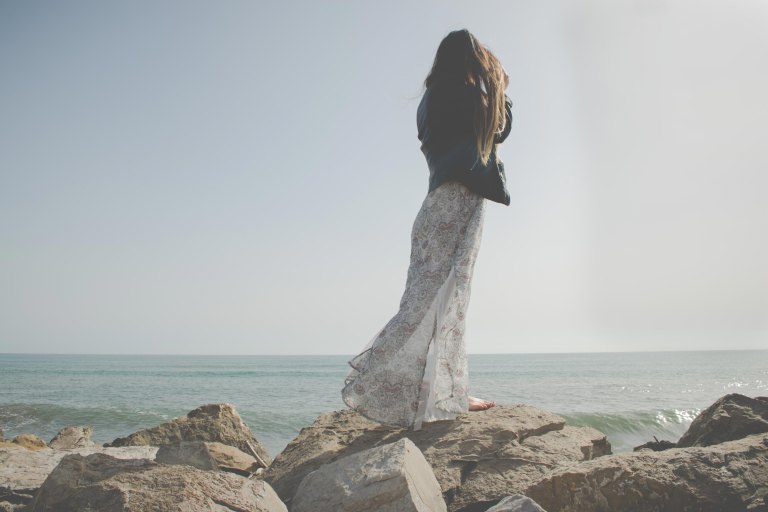 Woman in long skirt standing on beach rocks