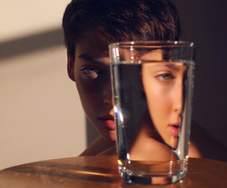 girl hiding behind drinking glass, scared to feel