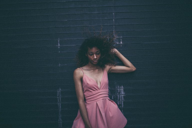 Woman in pink dress standing against wall