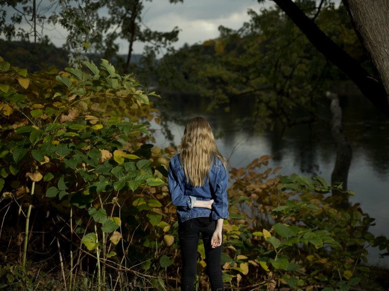 A woman stands alone in nature, looking distressed