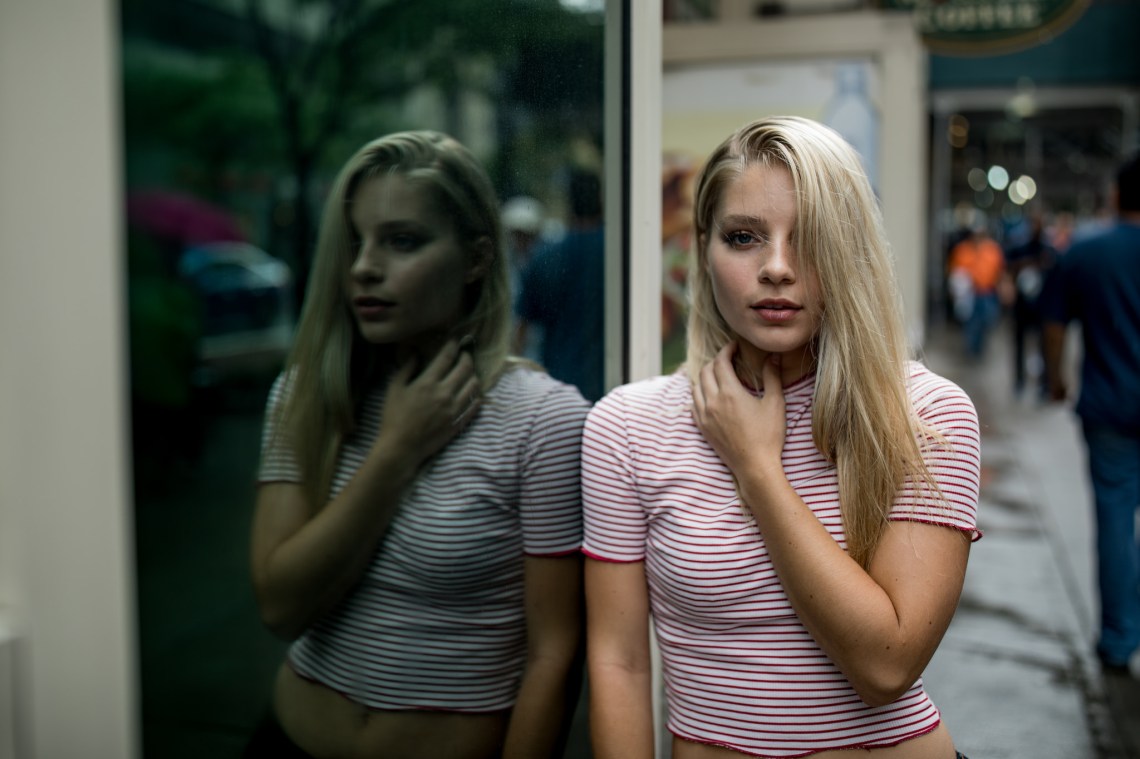 Woman stands by a window on a subway and stares straight into the camera