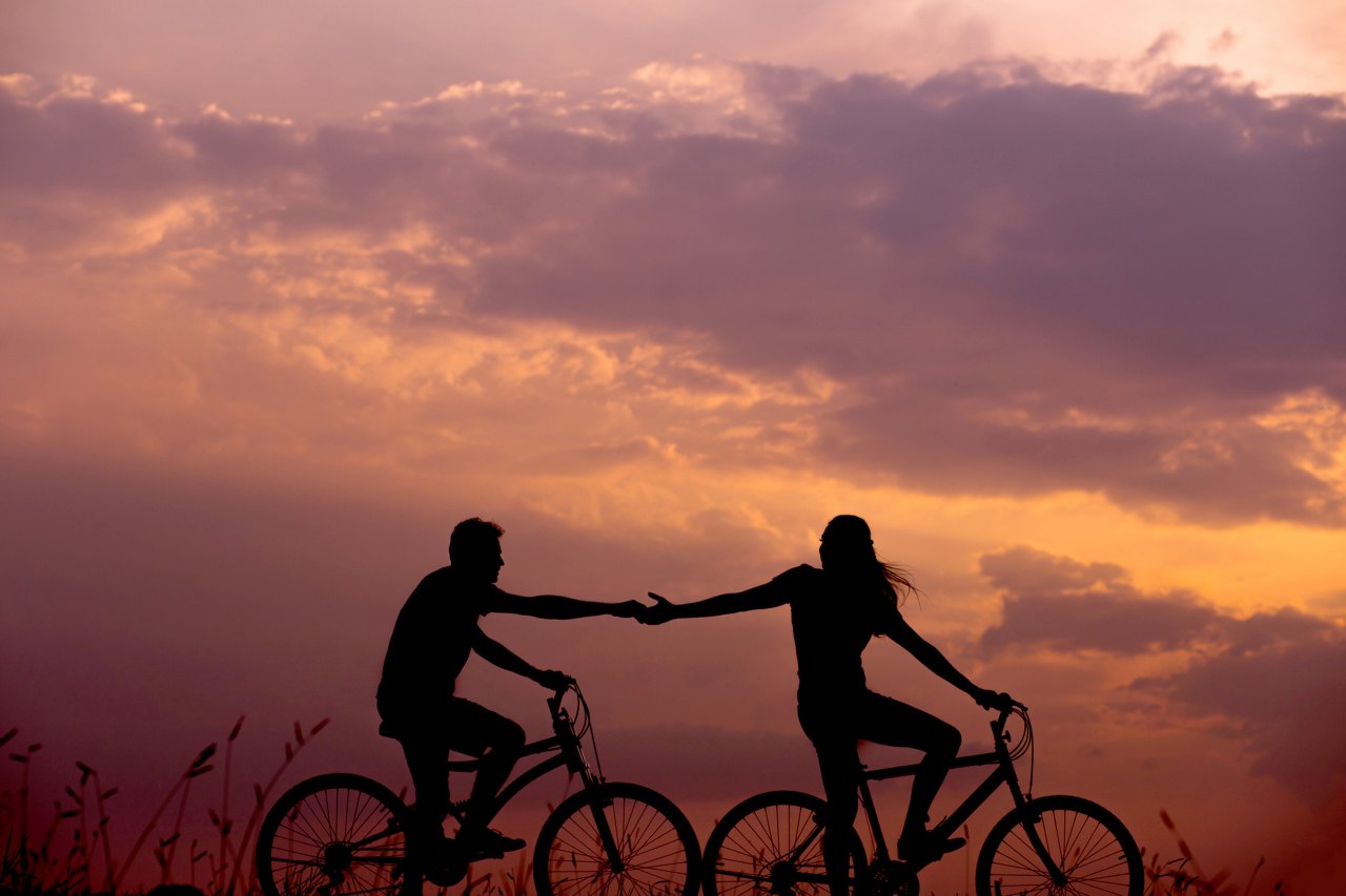 a woman and a man biking together while holding hands