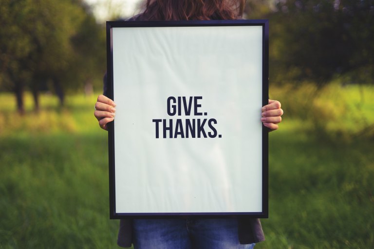 A woman holds up a sign that says "Give. Thanks."