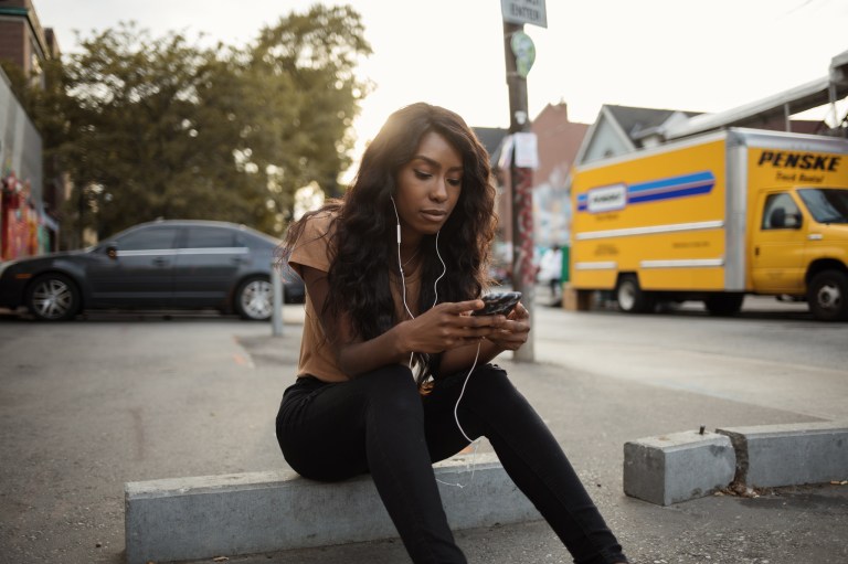 Occupied Young Woman Going Through Her Phone as She Listens to Music