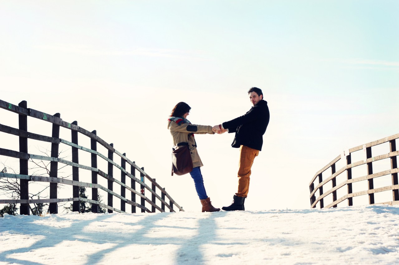 Man and woman hold hands on a snowy bridge