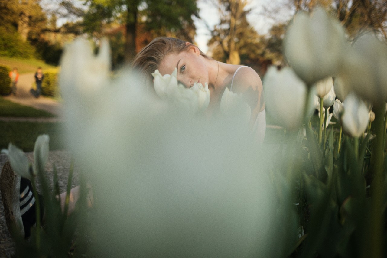 Beautiful young blonde gazing up seductively from behind white tulips