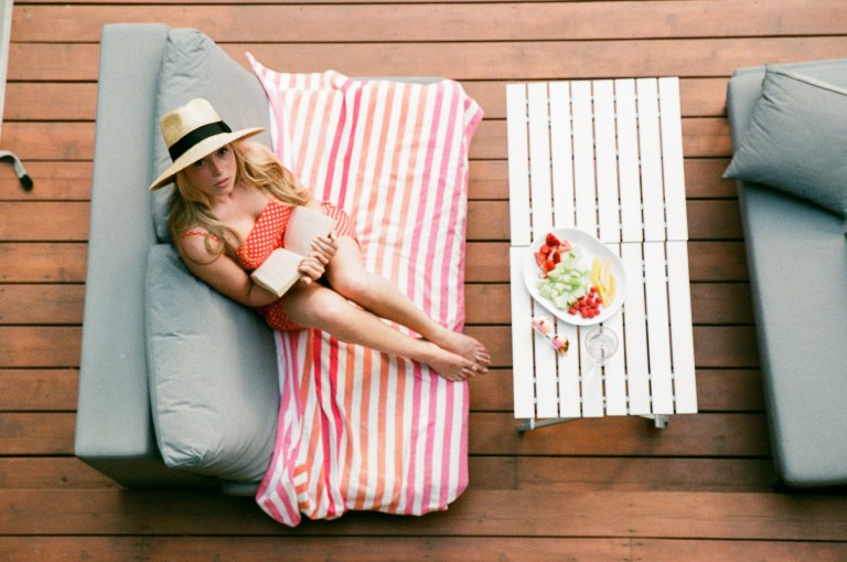 Woman in a red dress and sunhat looking up while reading a book