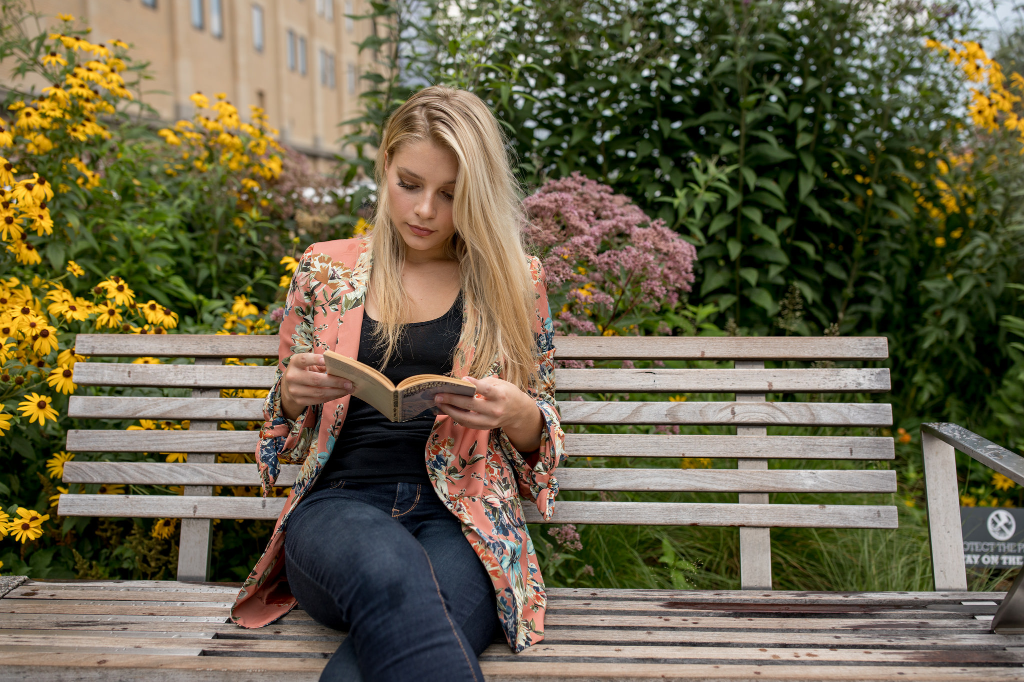 blonde young woman reading alone on bench