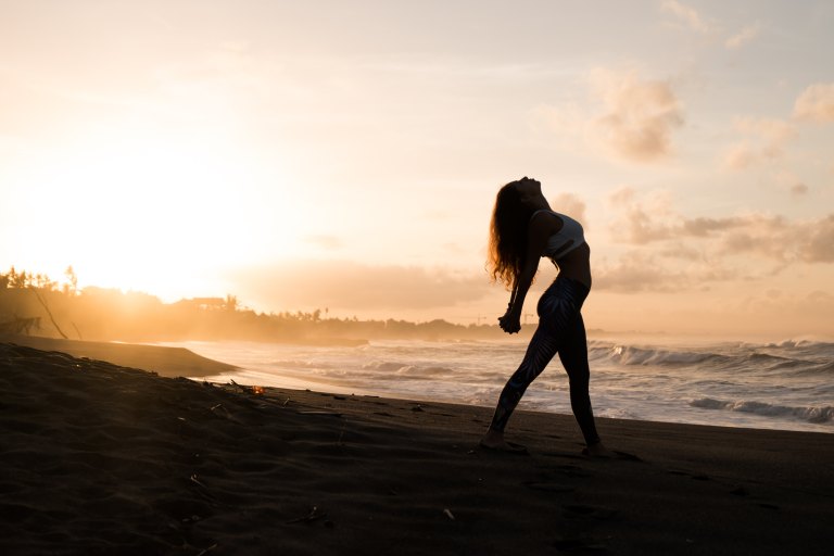 girl doing yoga by the ocean