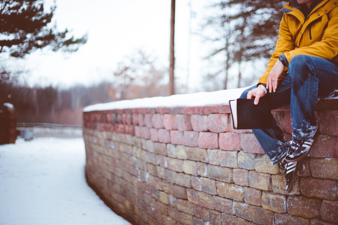 man sitting on snowy ledge with book