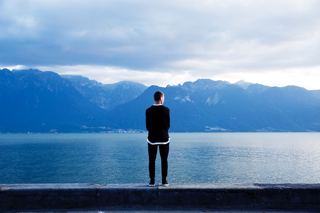 A man standing on a stone ledge and looking off into the mountain lake