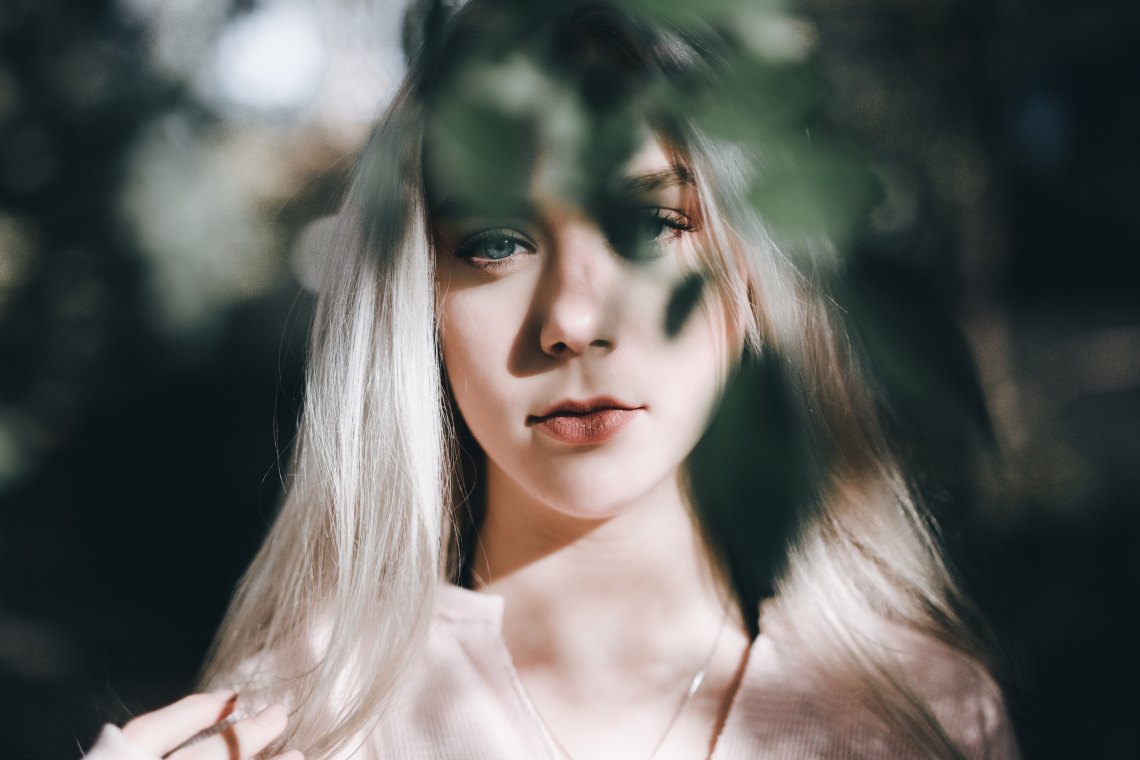 blonde girl staring at the camera behind leaves 