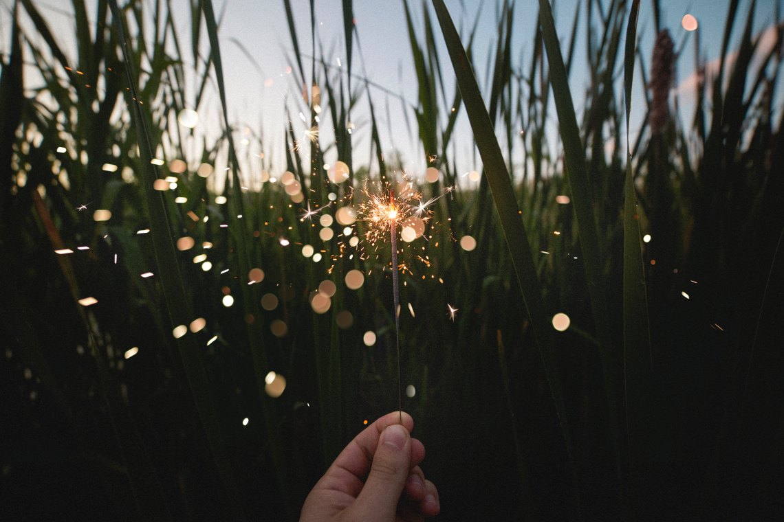 a hand holding up a sparkler in front of grass 