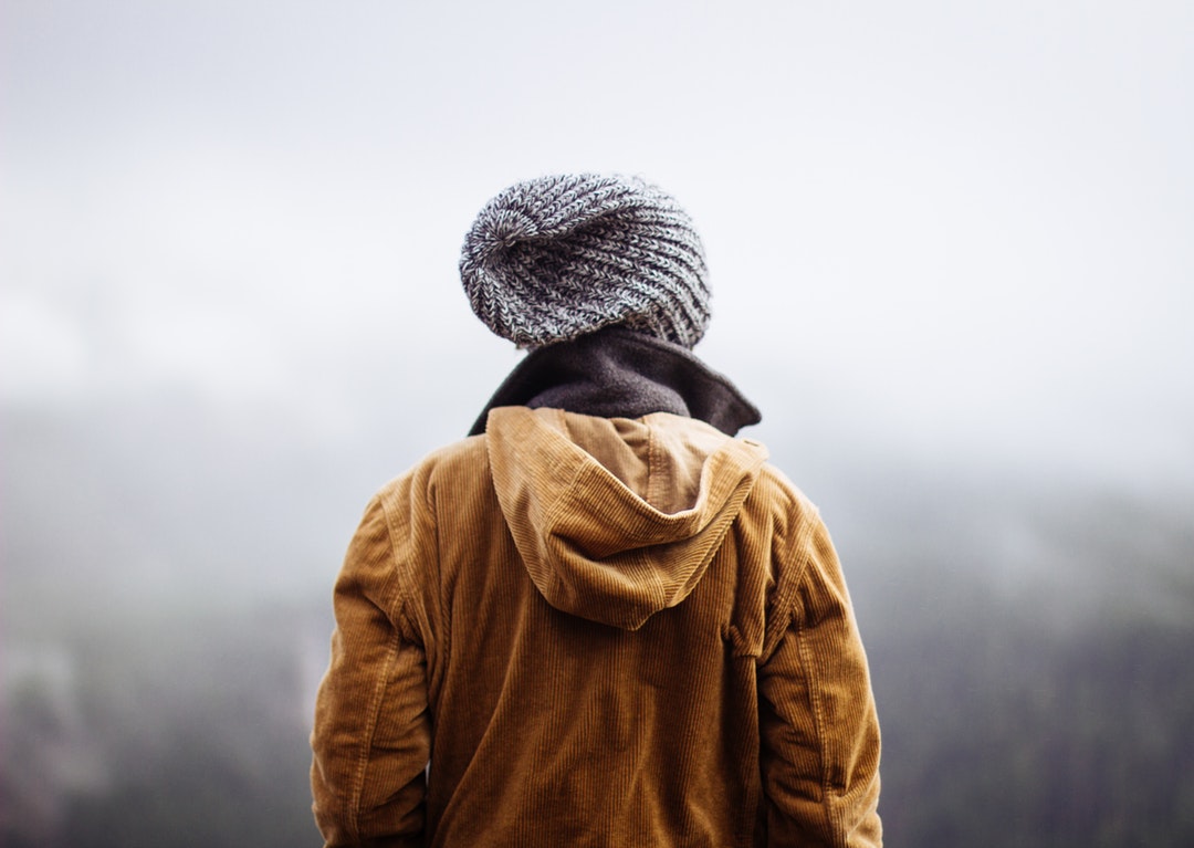 Person in winter jacket looks out a foggy forestscape on a hike