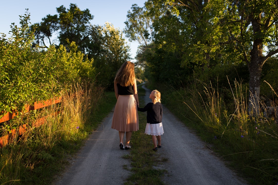 Child and mother walk through park trail as shadows lengthen