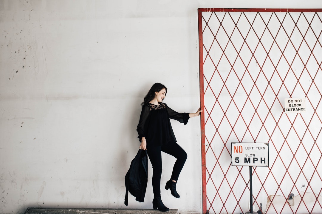 A woman dressed in black is holding onto the entrance gate next to the signs.