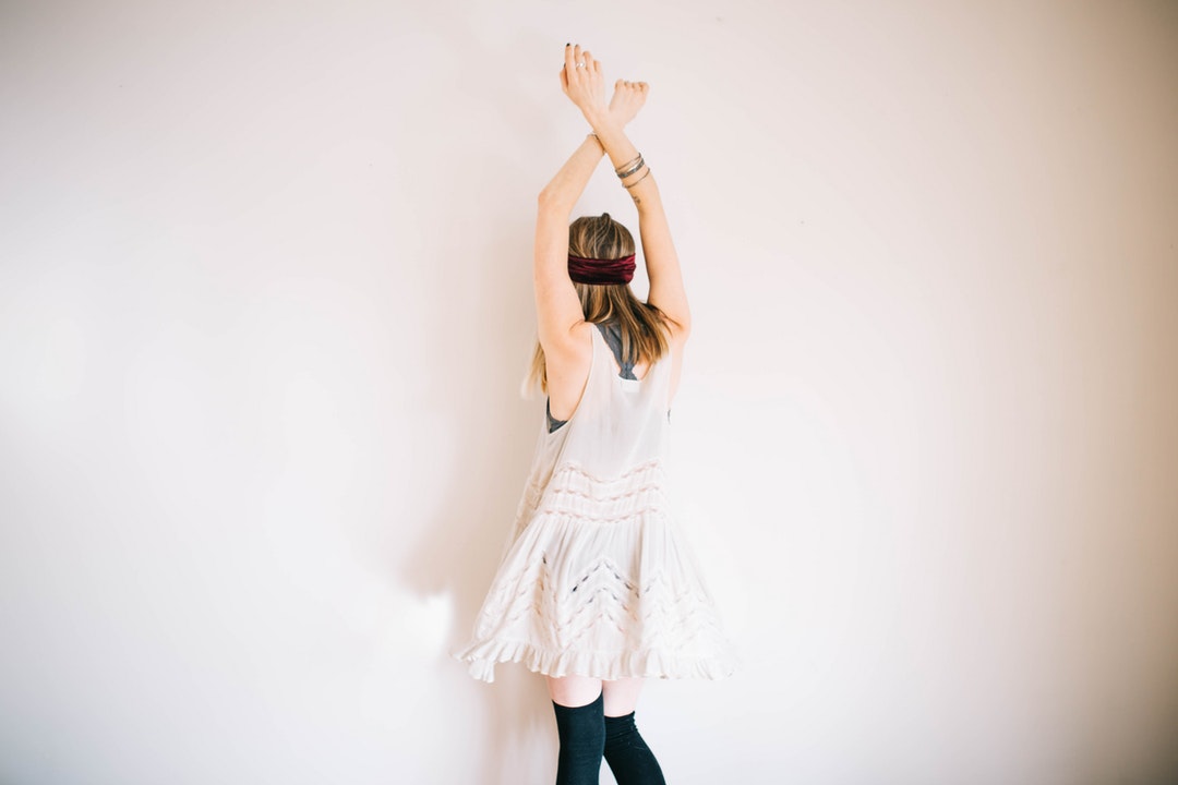 A woman in a white dress and black knee socks dancing near a wall