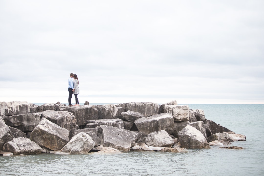 Standing on a stone jetty on the ocean, a couple shares a tender moment