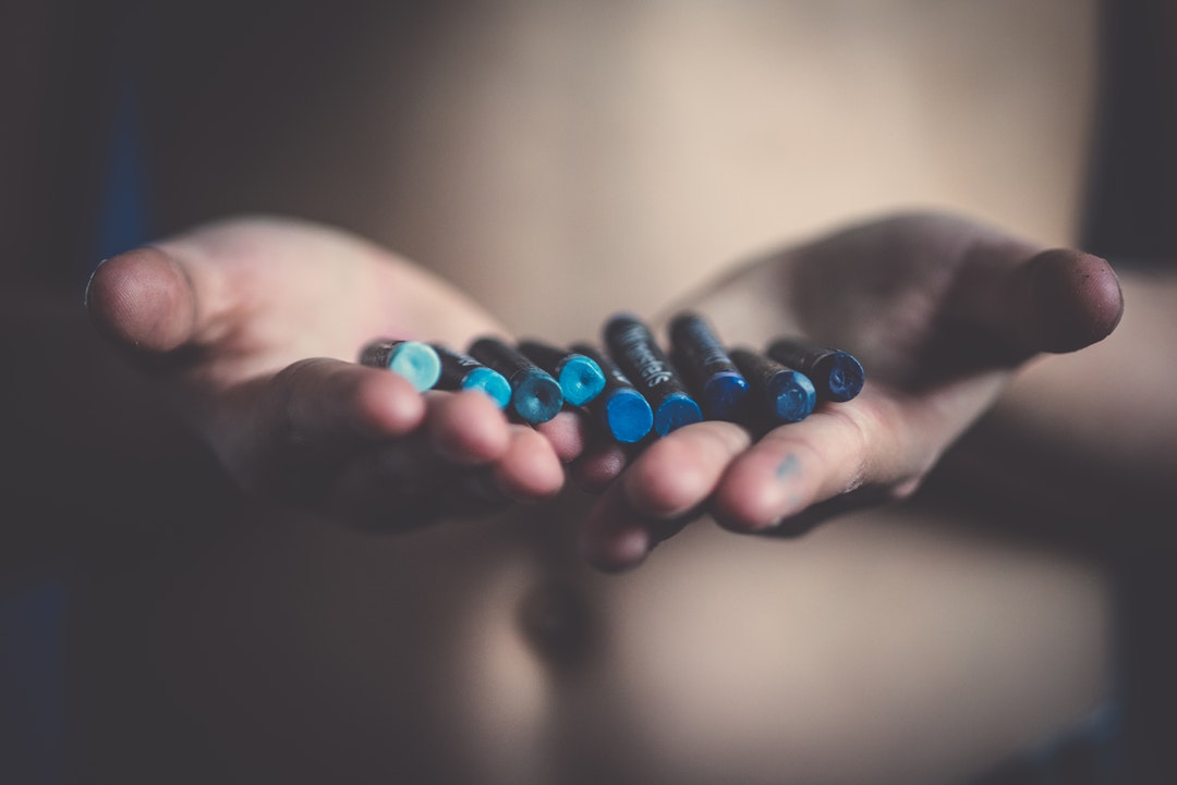 Open hands holding blue crayons with dark lighting in Brussels