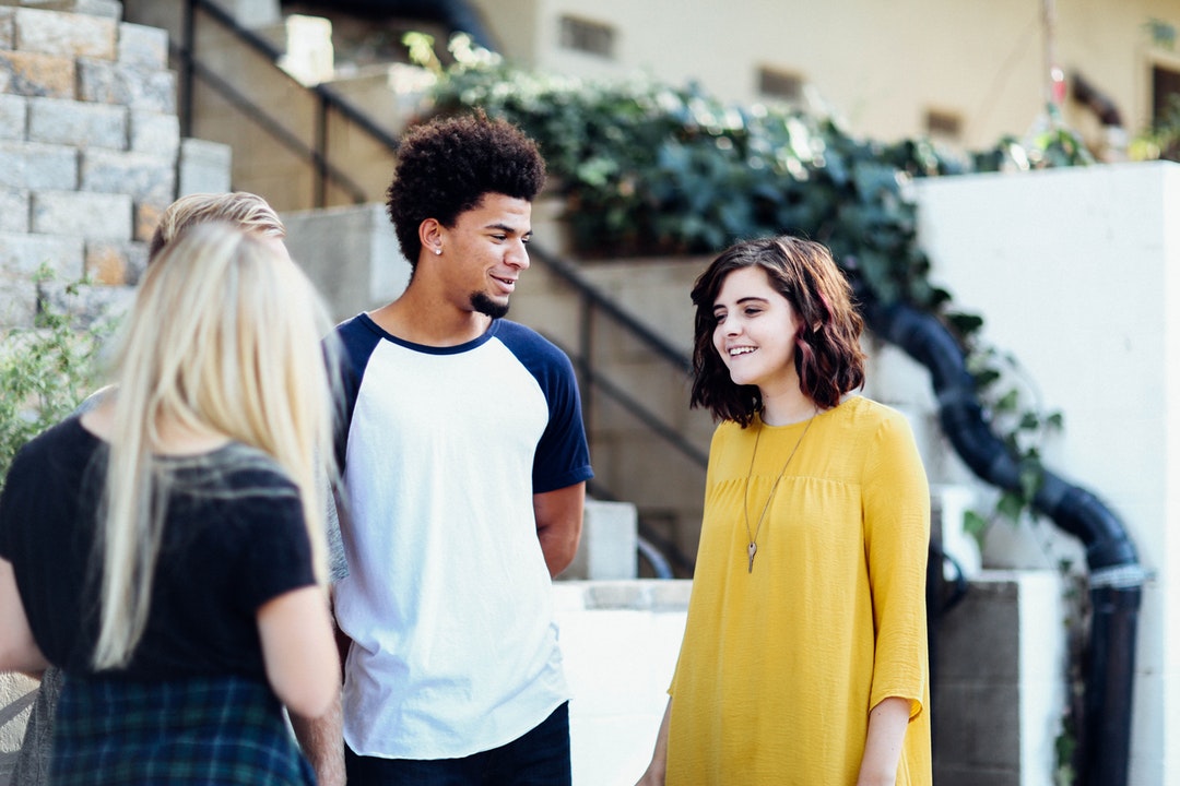 Four young people smiling while talking near a staircase outside a building