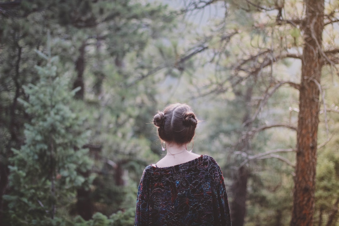 A woman with her hair up in buns walking through an evergreen forest