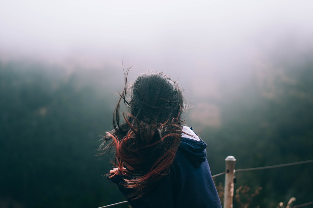 A girl's hair moving in the wind as she looks out at a fog covered San Francisco