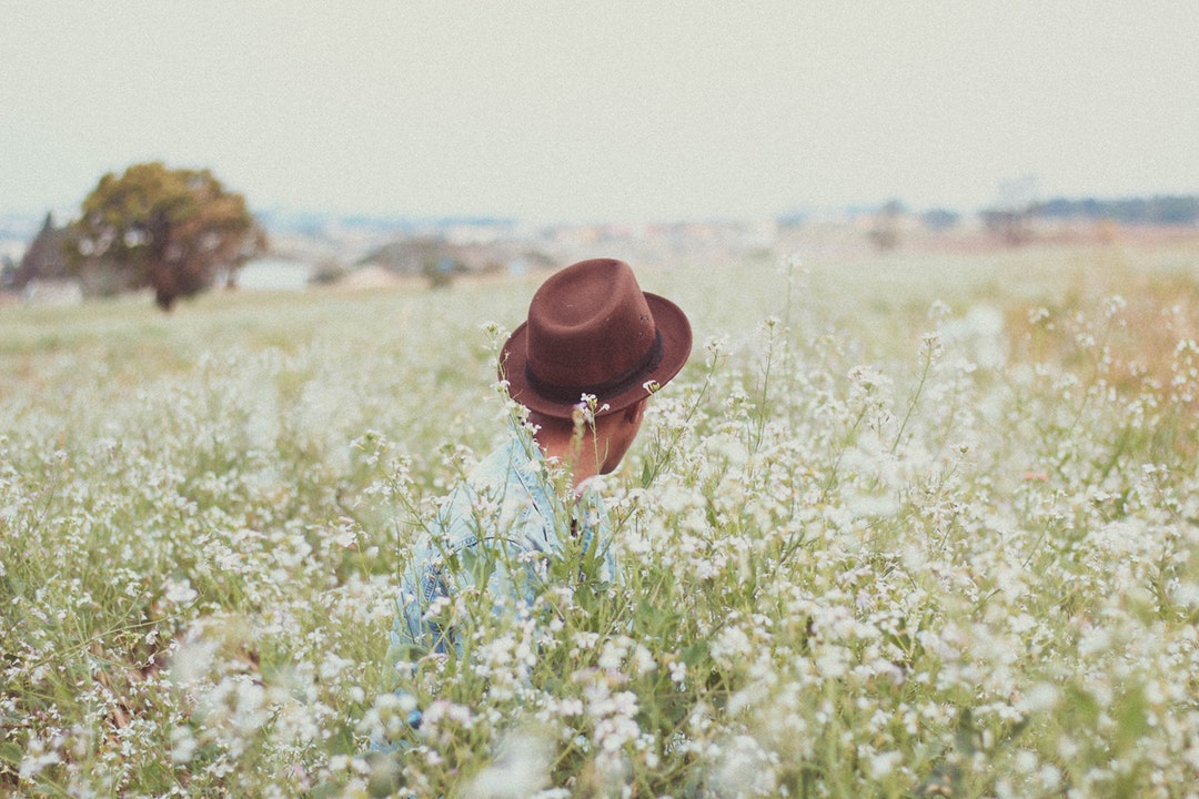 Person in a brown hat sitting in a field of wildflowers