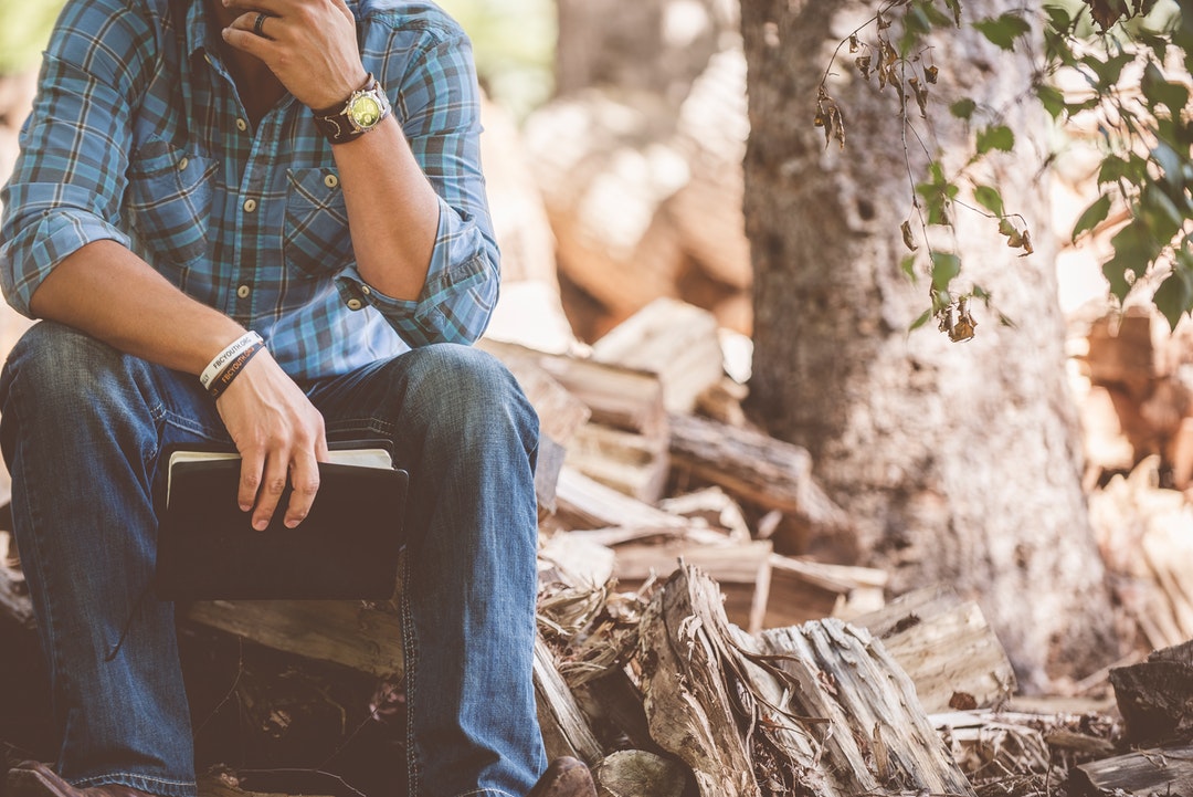 A thoughtful man with a notebook sitting on a pile of firewood