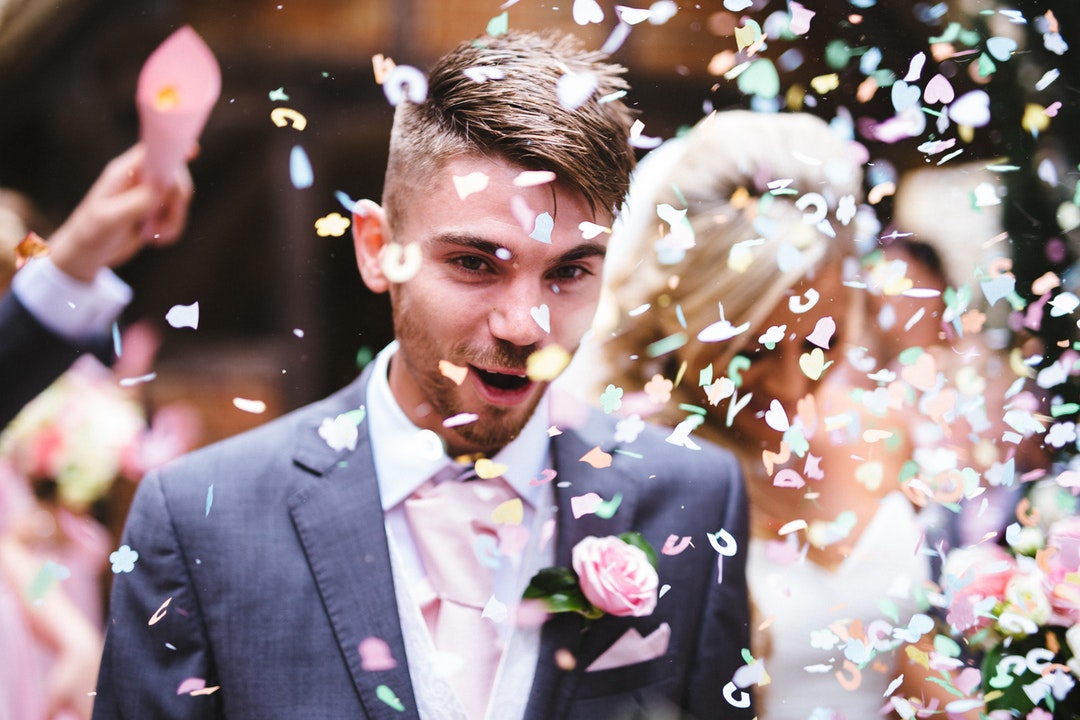 Confetti is thrown over excited groom leading the way for bride after Ash Vale wedding