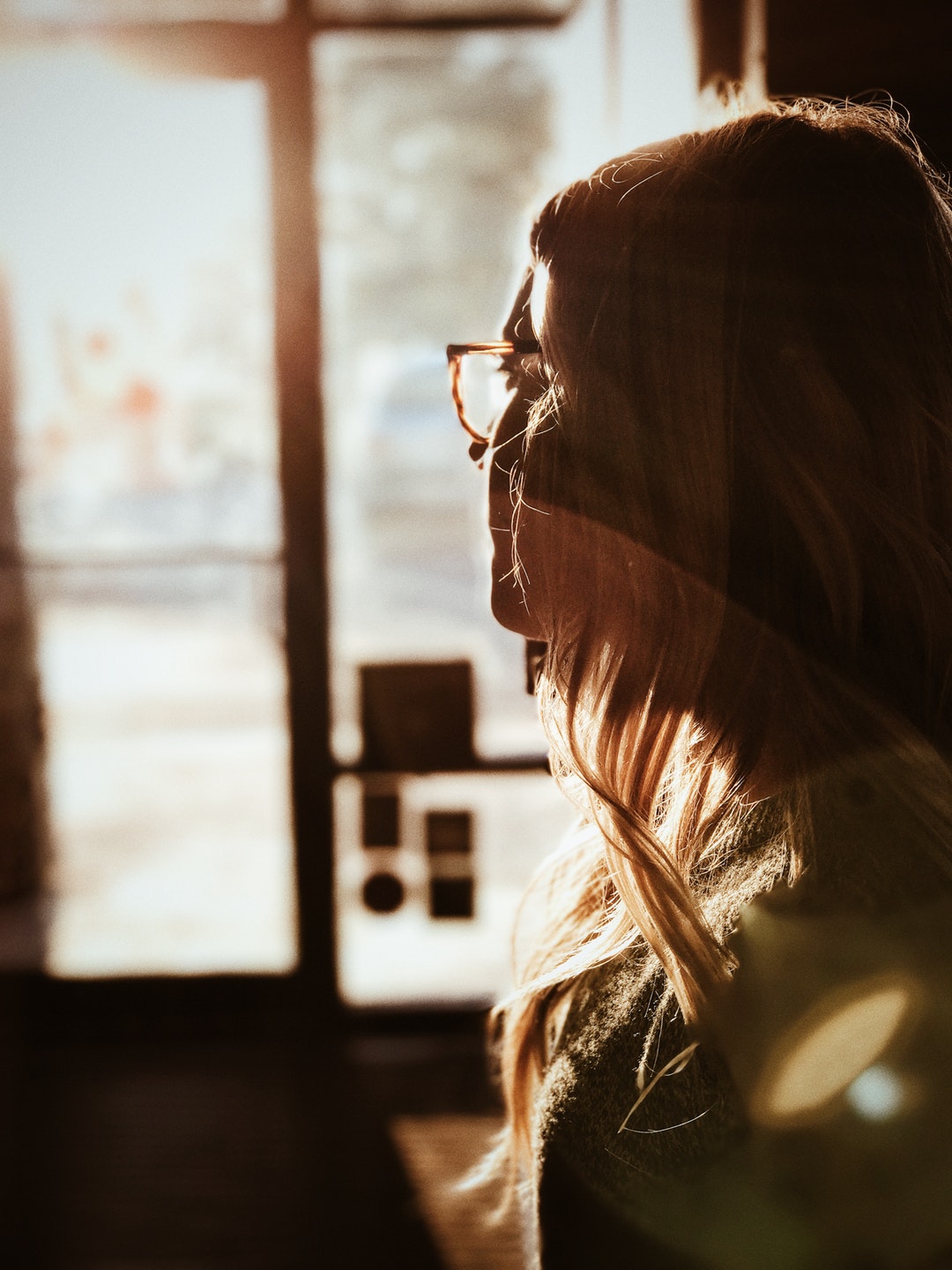 A blonde woman in glasses longingly looking at the window