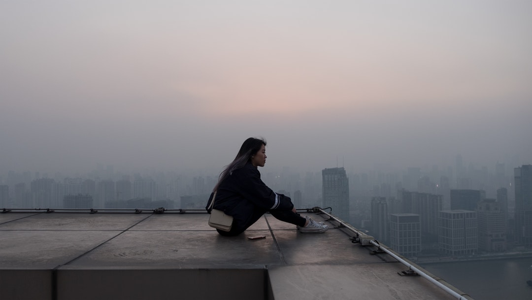 A woman sits looking into the foggy distance atop a building in Shanghai