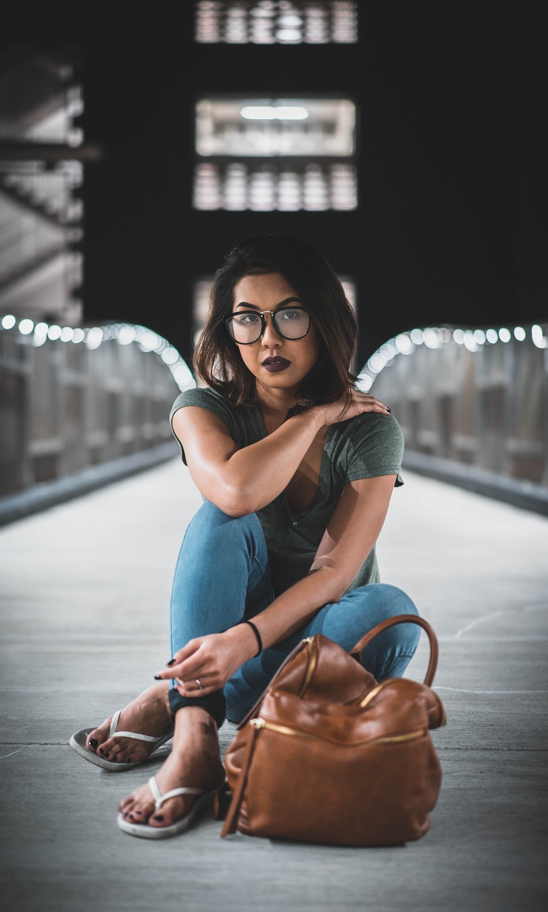 A woman with dark hair and eyes wearing dark lipstick sitting on a lit up bridge