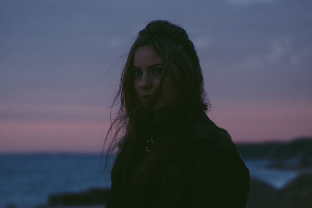 Woman with windblown hair standing near an ocean at dusk