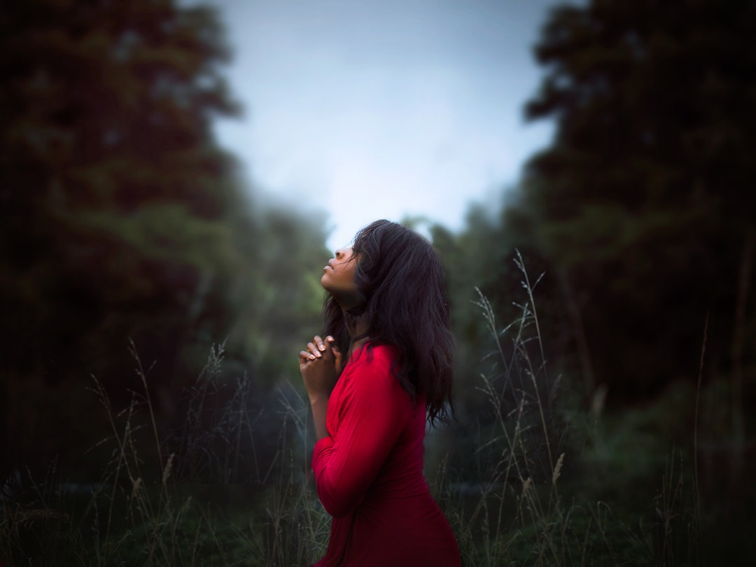 Pensive woman standing in a field praying and thinking