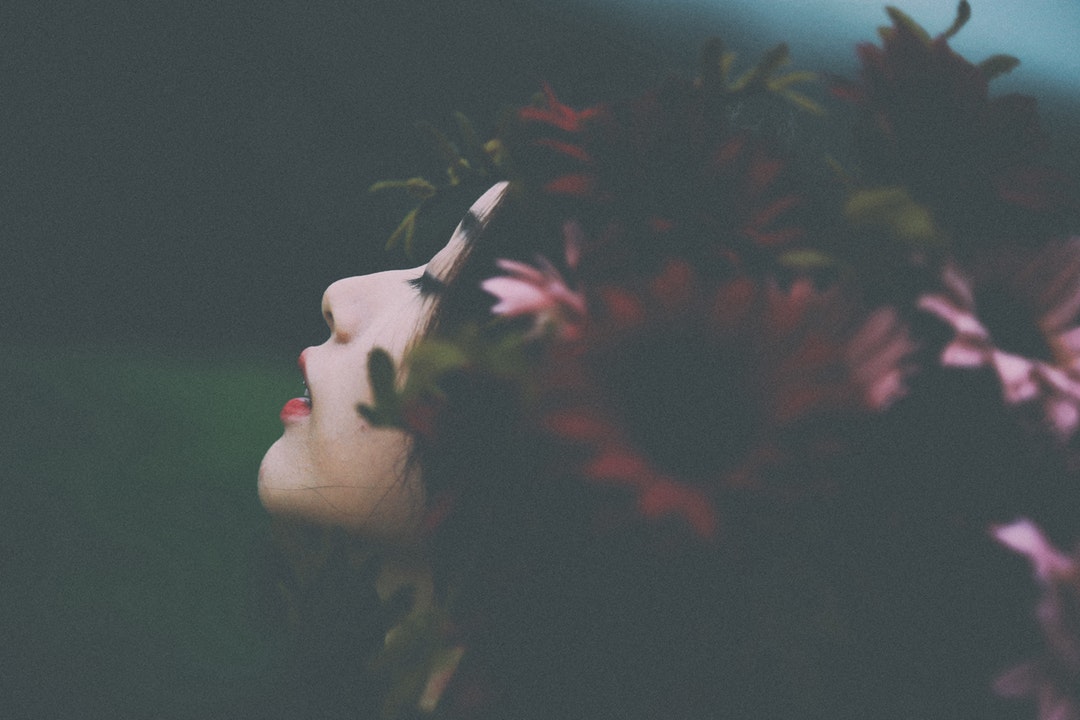 Young Asian woman with flowers in her dark hair with face uplifted and eyes closed expectantly