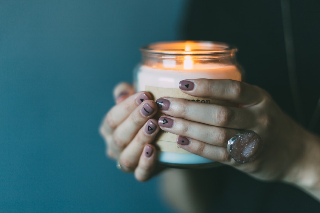 Woman wearing stone ring and painted nails holds lit candle in dark light