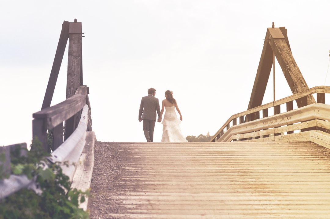 A man and woman in wedding attire are walking on a bridge in London.