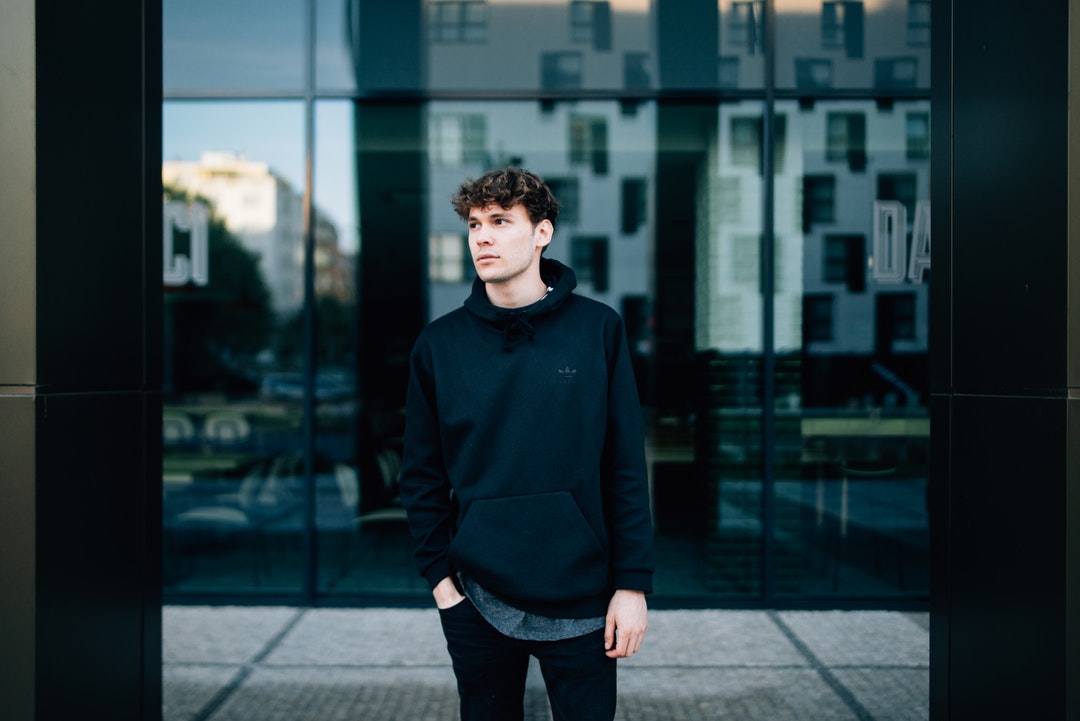 Man in a balck hoodie stands in front of a reflective store window