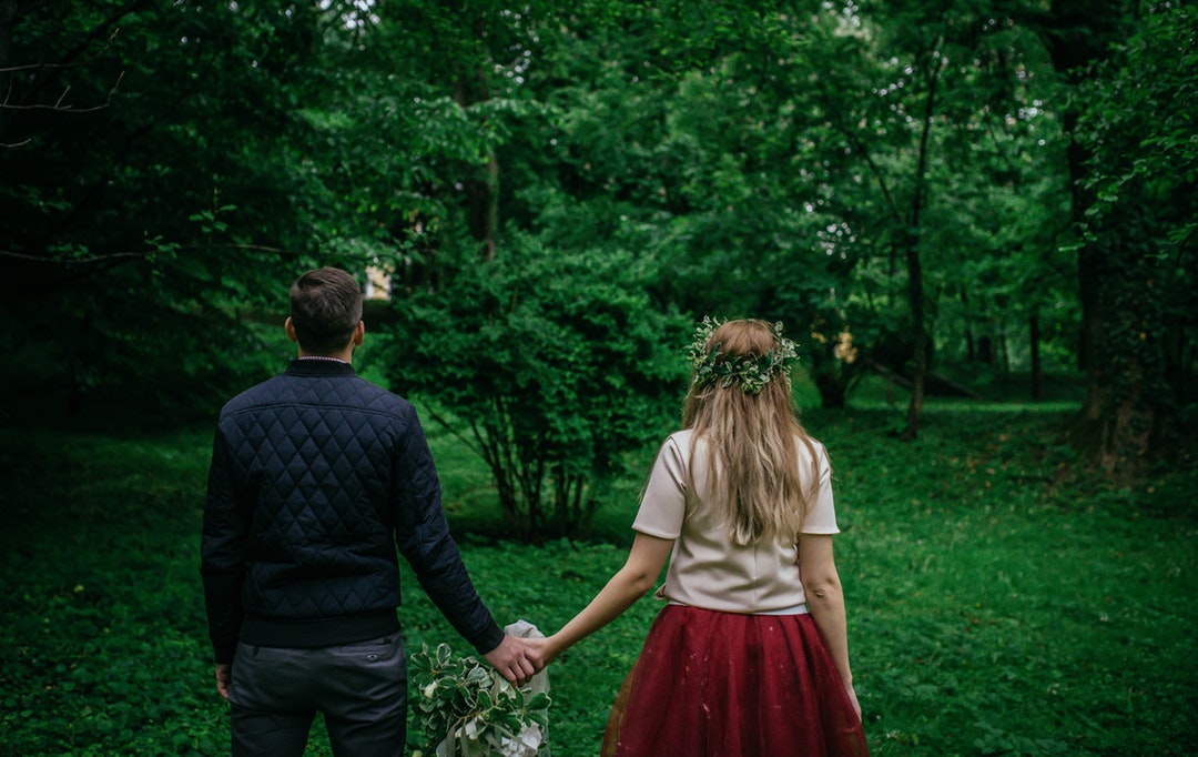 woman and man standing holding hands facing trees