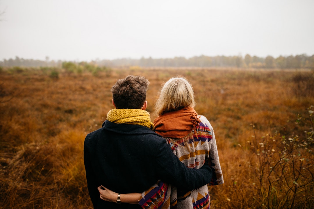 couple standing on brown grass field near tall trees at daytime