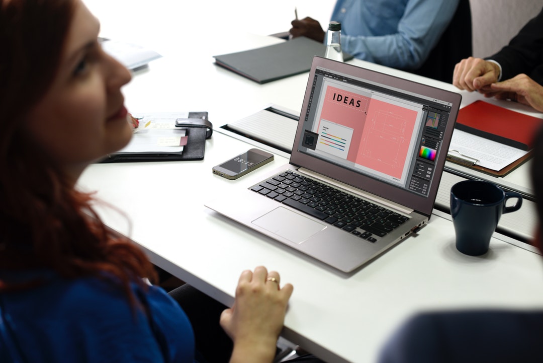 A woman sitting at a laptop with an “Ideas” slide on its screen in a conference room