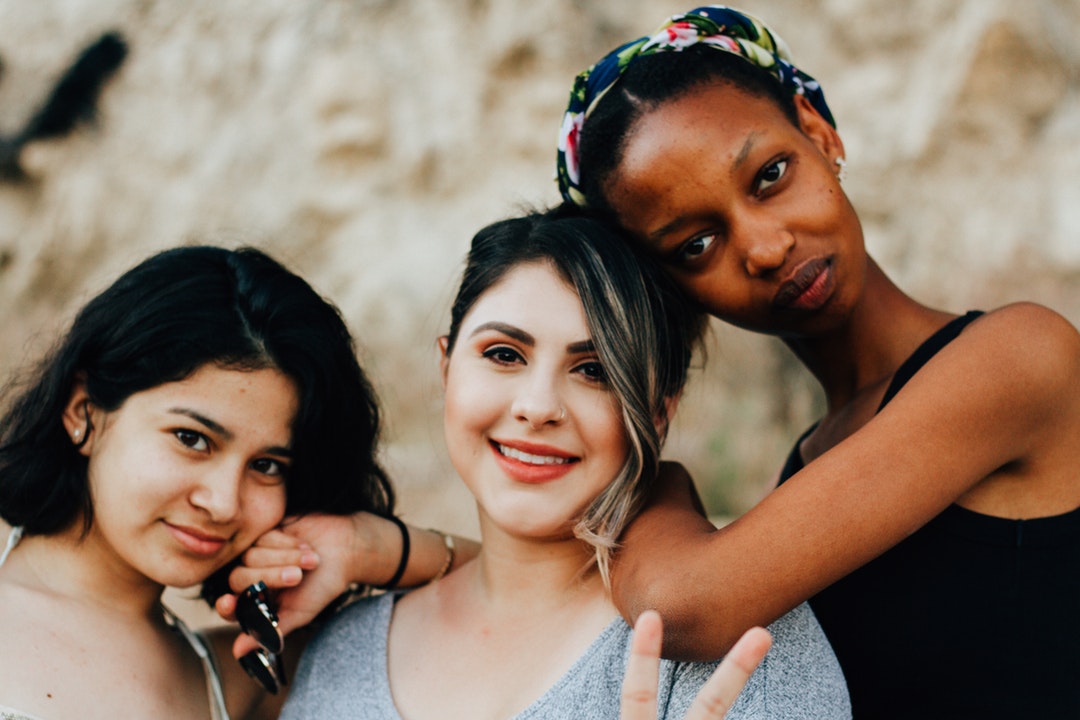 Three friends lean against each other at Running Springs. One smiles, holding up a peace sign.