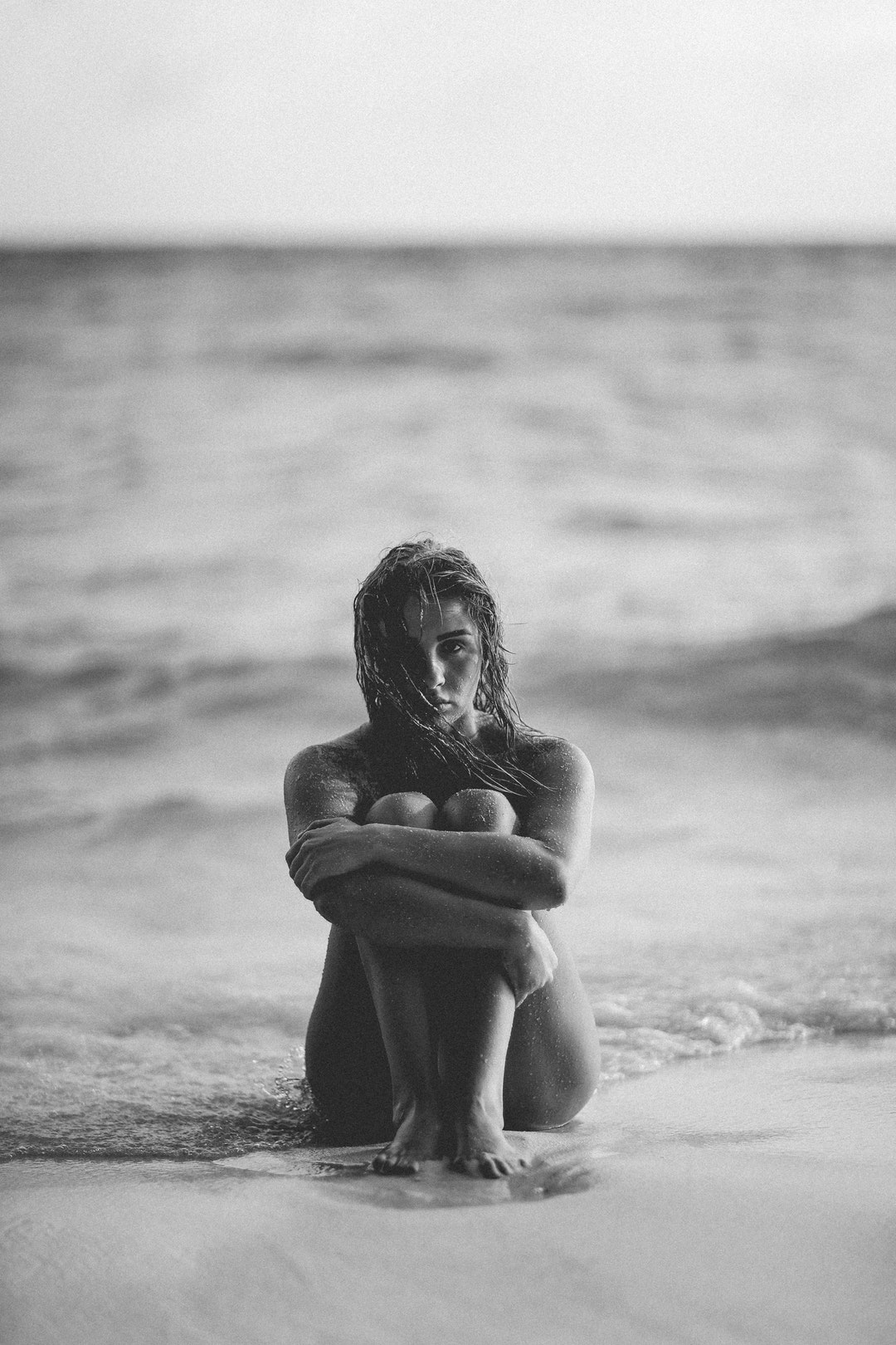 Black and white shot of attractive woman sitting with knees up on beach in Maldives