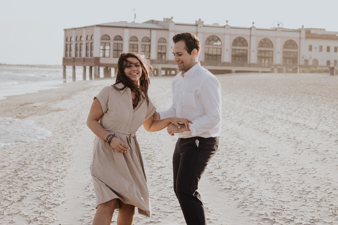 A smiling couple touches hands in the wind on the beach at the Ocean City Boardwalk