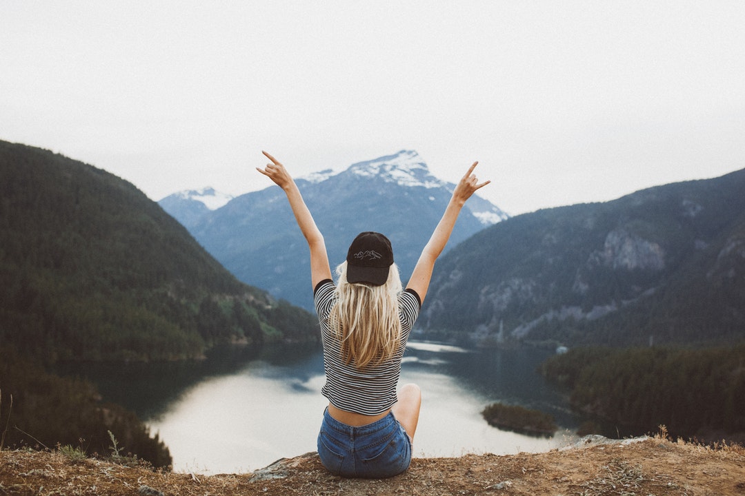 A woman sitting on a cliff over a mountain lake.